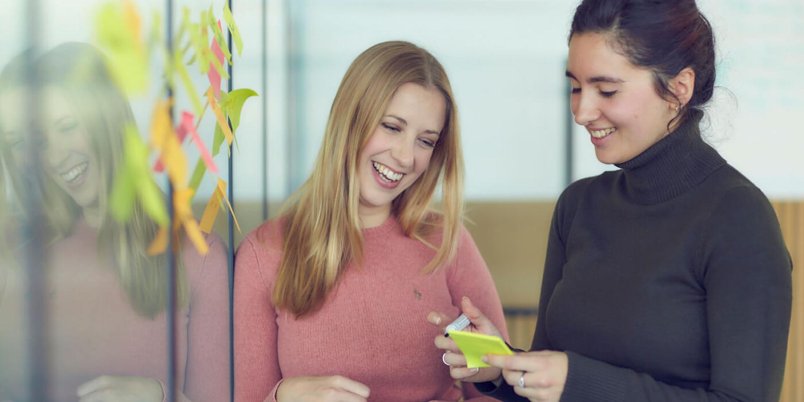 Two women smiling and writing on post-it notes